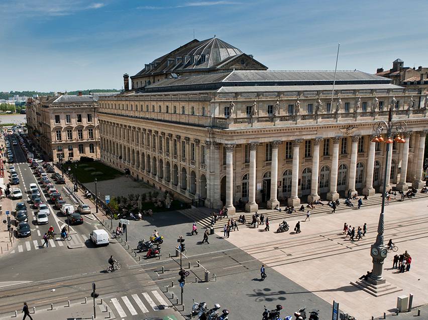 Luftfoto af Grand Théâtre de Bordeaux med mennesker og biler på gaden.