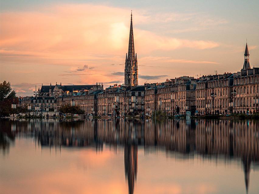 Bordeaux's bybillede ved solnedgang med en kirke og dens spejling i vandet.
