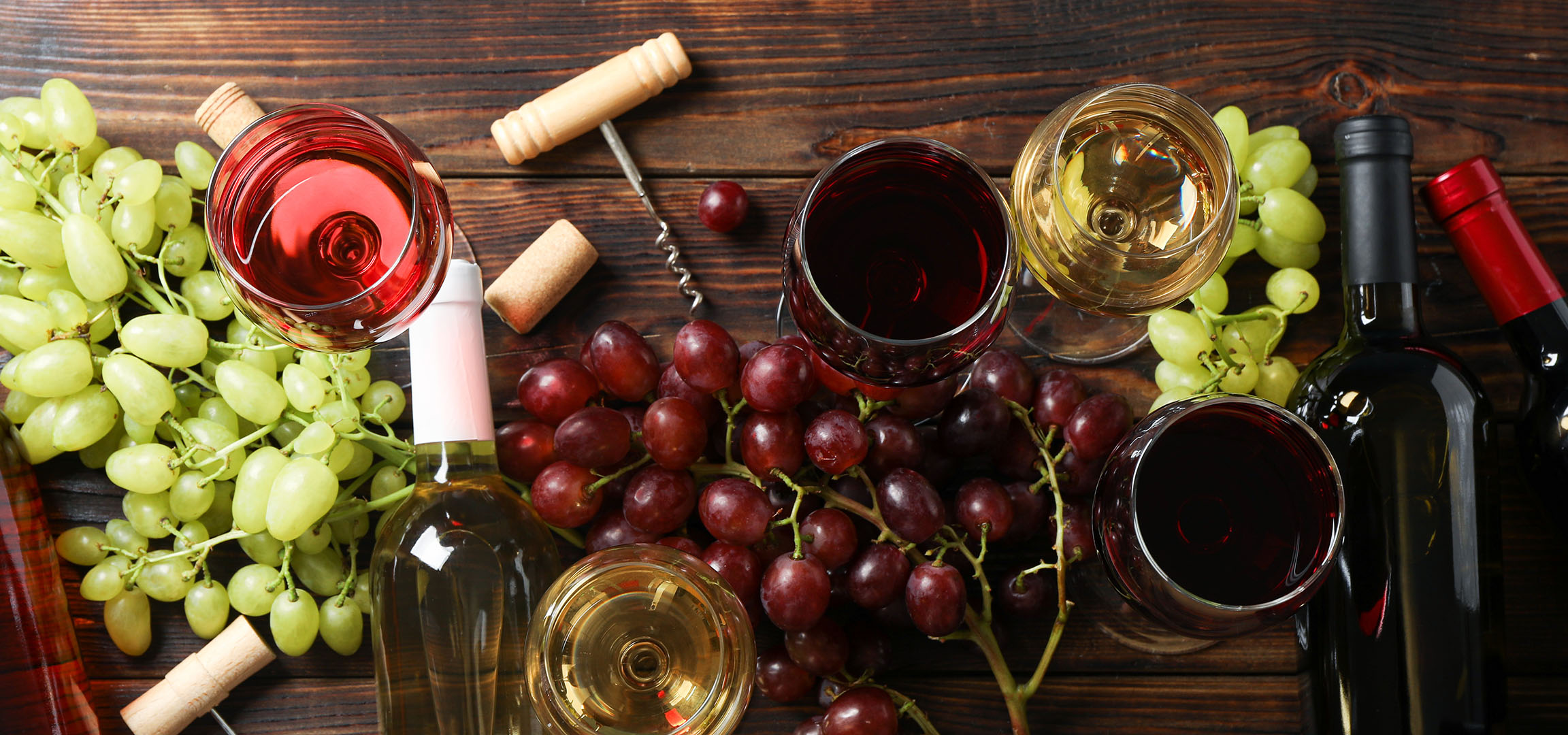 Forskellige vine, druer og vintilbehør på et træbord.