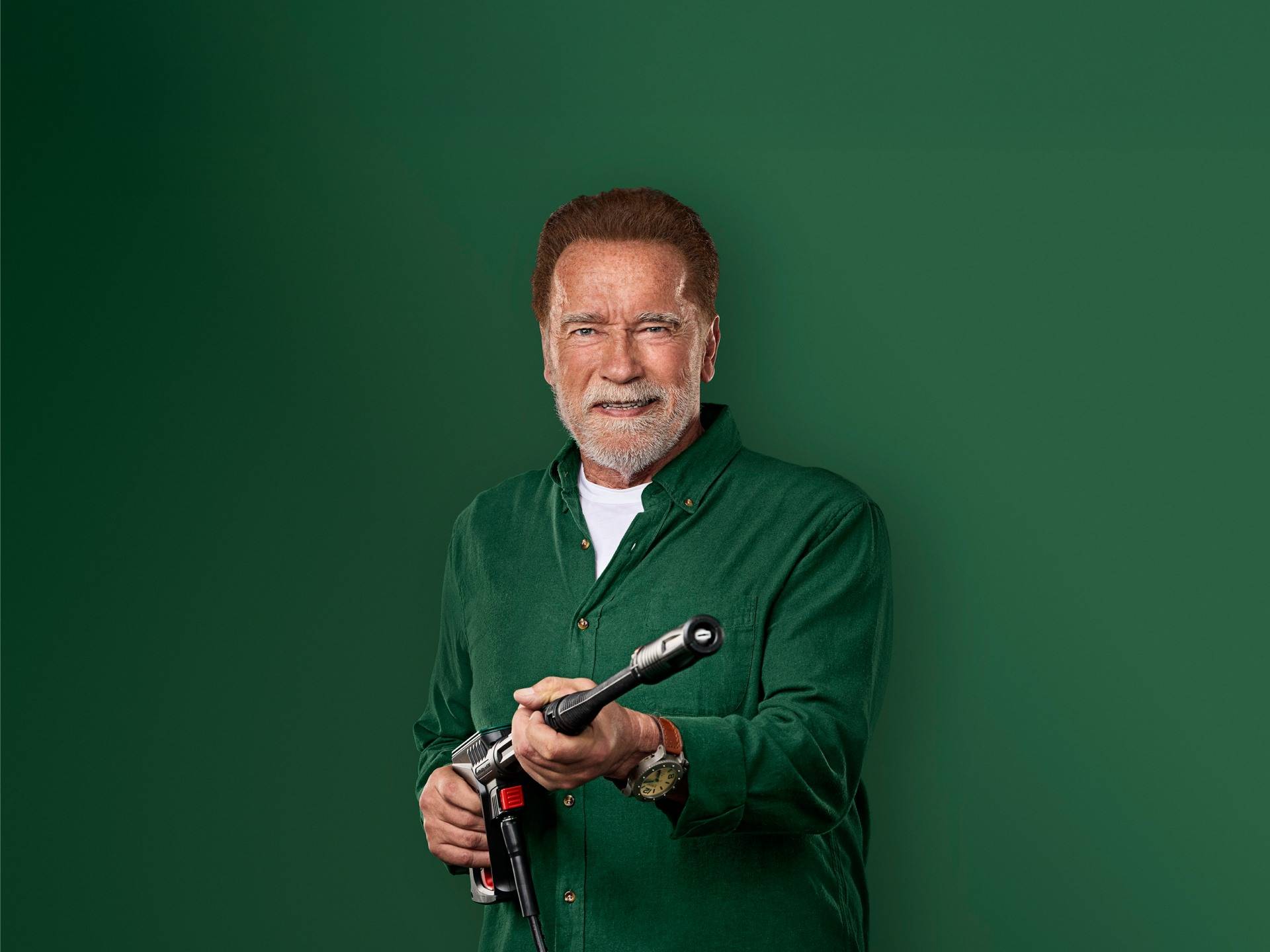 Arnold Schwarzenegger smiler, holdende en højtryksrenserpistol.