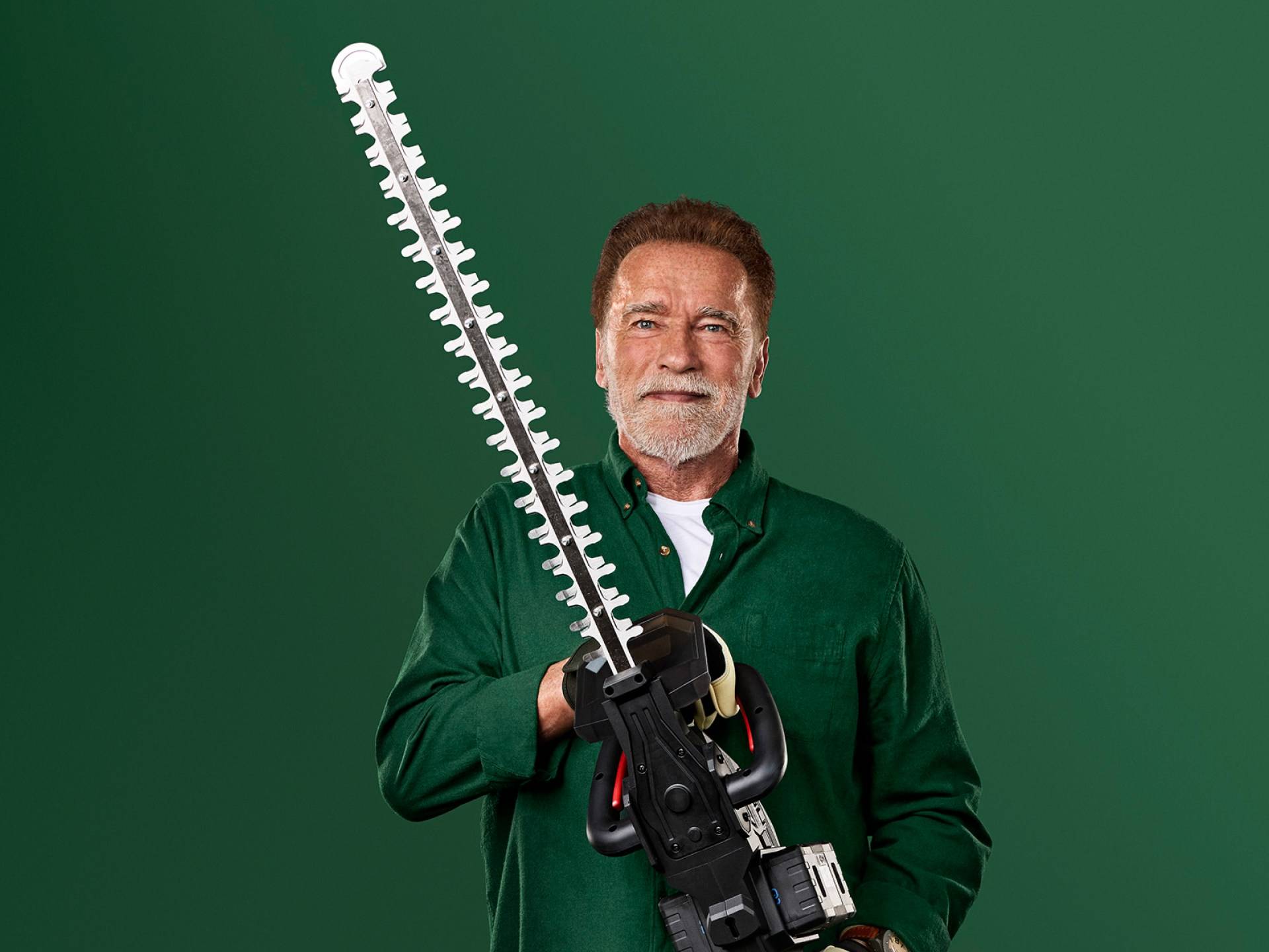Arnold Schwarzenegger holder en stor hækkeklipper mod en grøn baggrund.