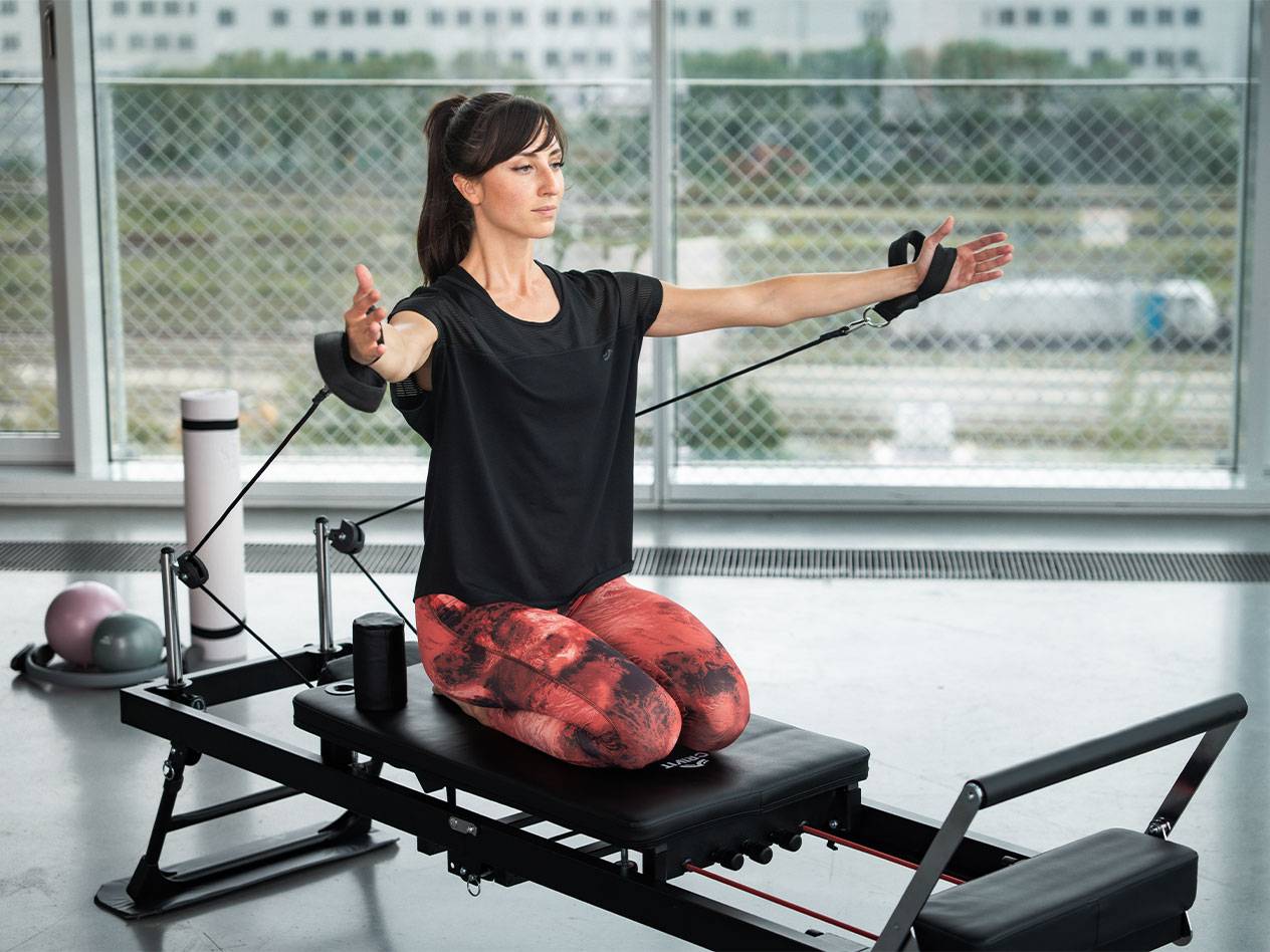 Kvinde laver Pilates på en reformer med modstandsbånd.