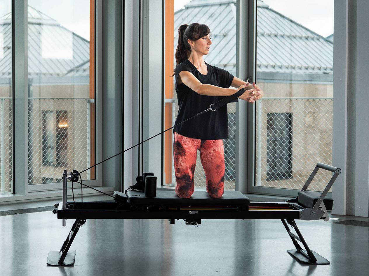 Kvinde dyrker Pilates på en sort reformer-maskine i et lyst rum.