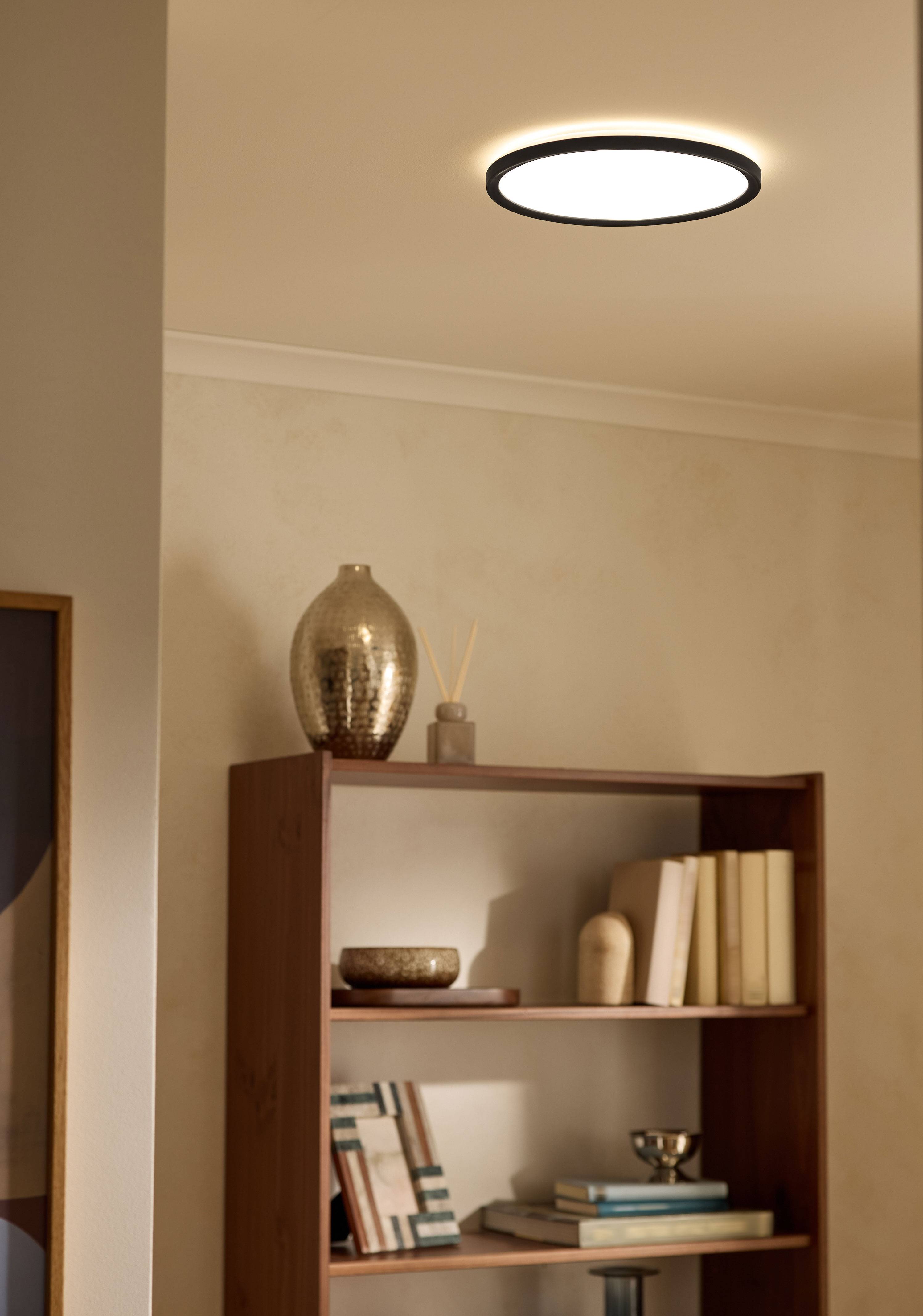 Loftlampe oplyser en stuebogreol med bøger og dekorative genstande.
