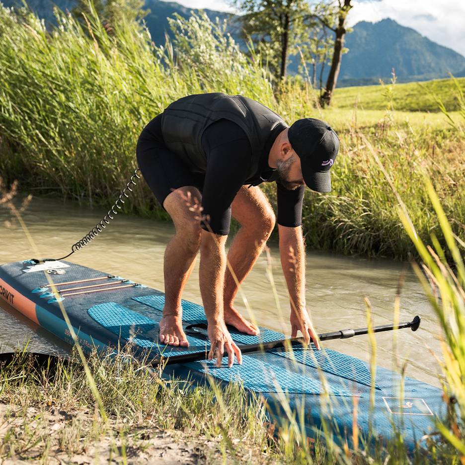 Mand i våddragt og redningsvest gør klar til stand-up paddling på en flod.