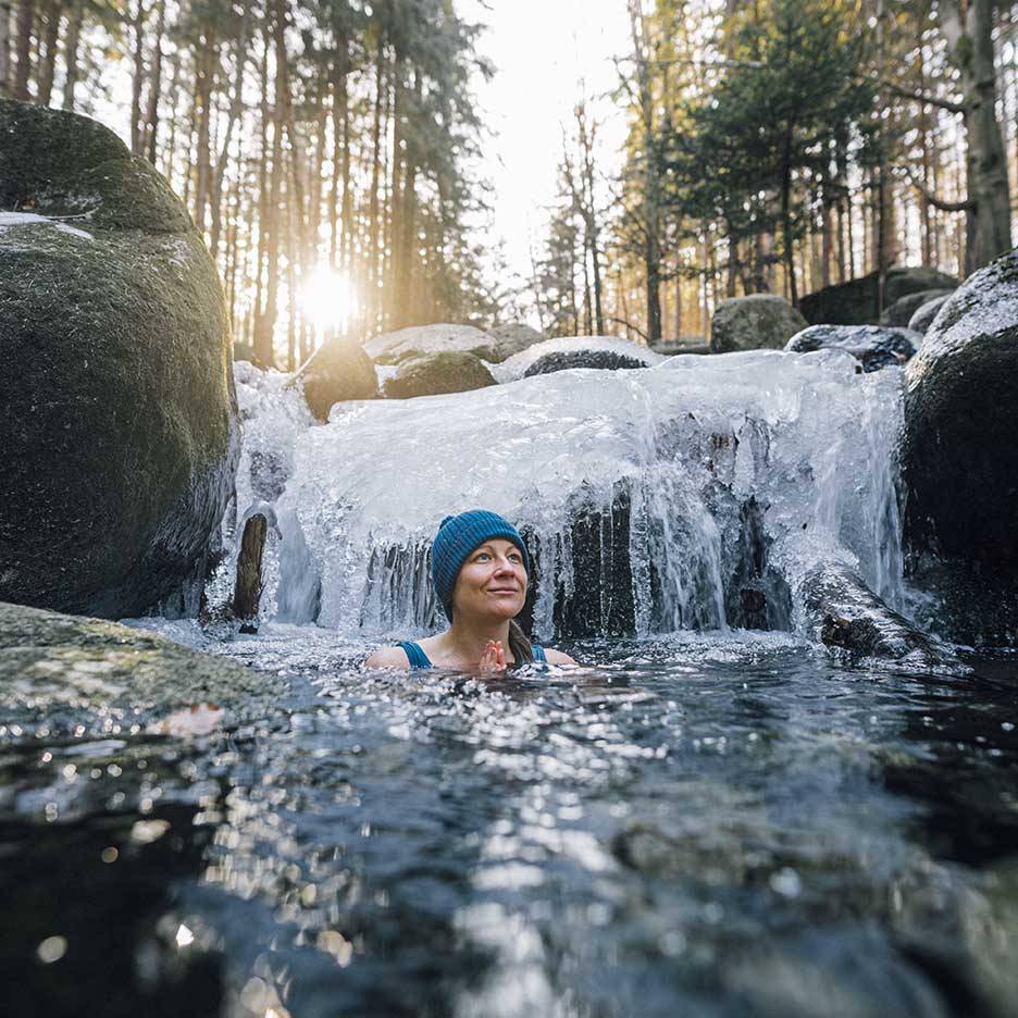 Kvinde i blå hue og badedragt nyder et koldt dyp i en frossen flod.