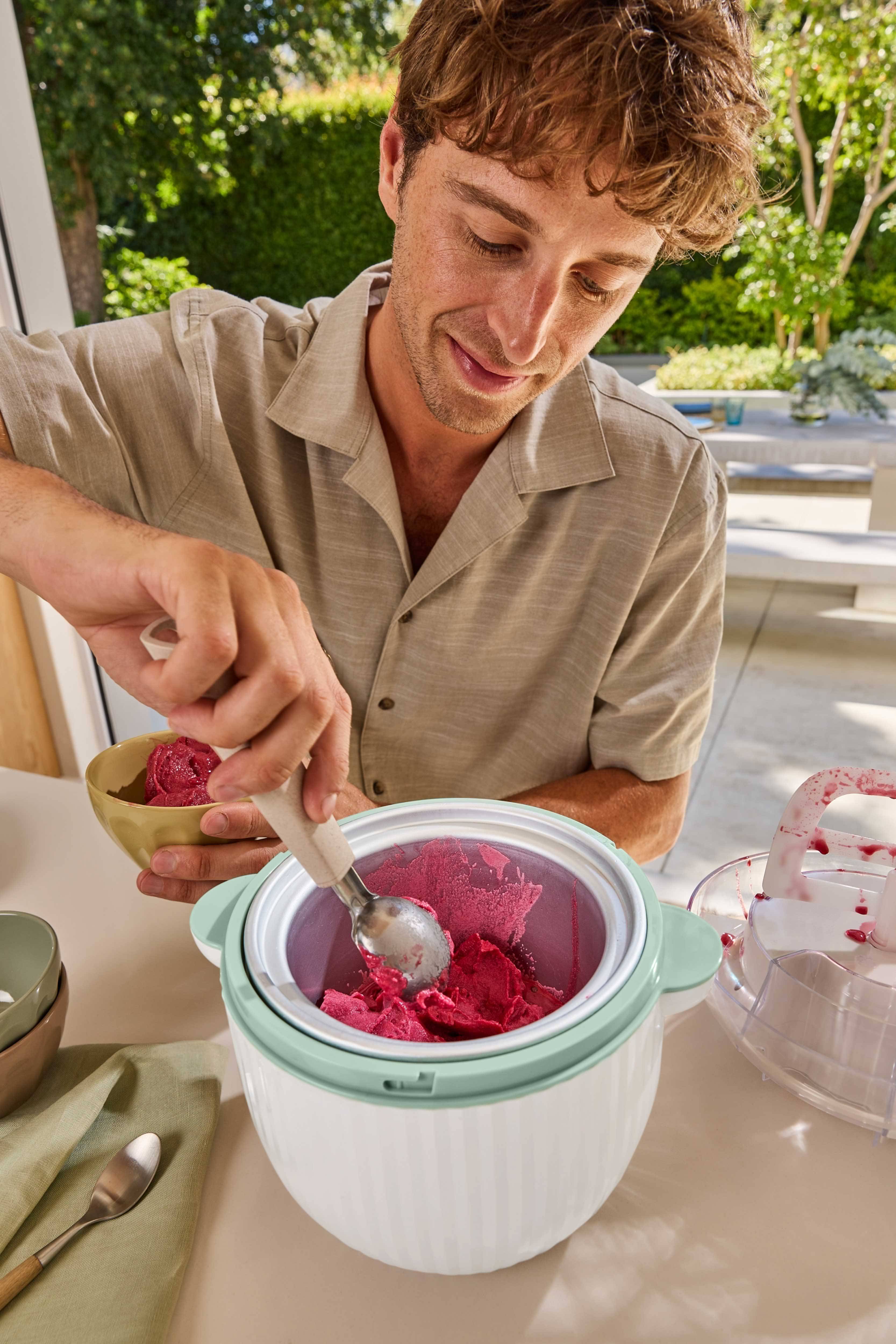 Mand skovler rød sorbet fra en ismaskine ned i en skål.