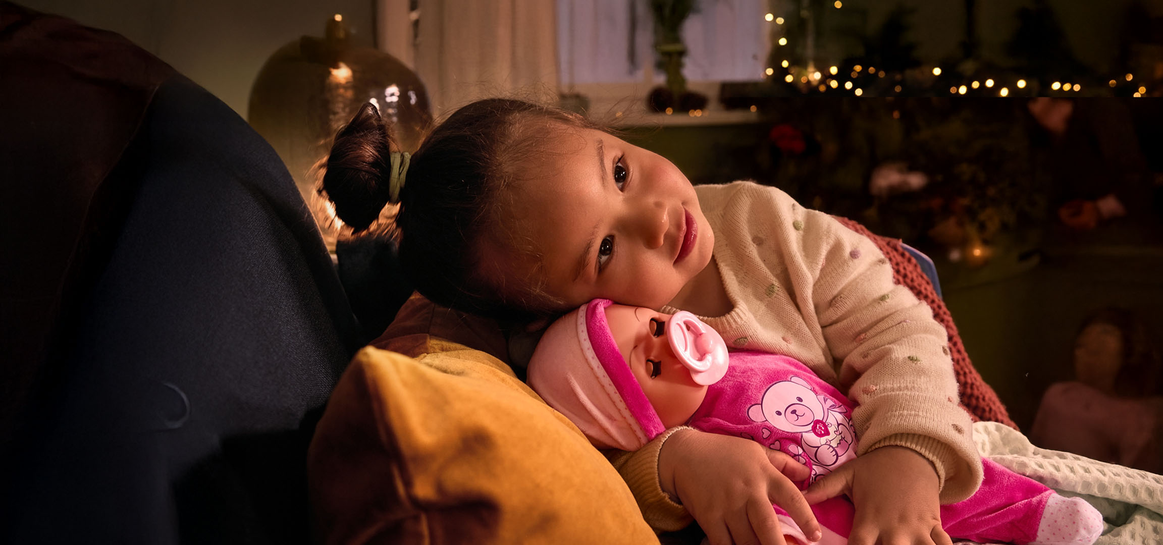 Pige med dukke og sut, hyggeligt placeret på en pude.