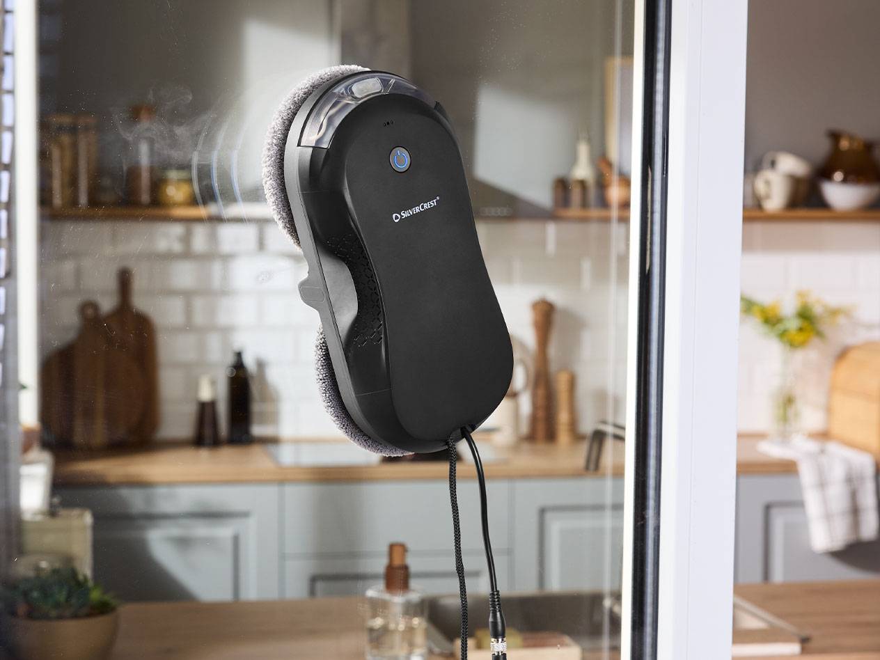 Silvercrest vinduespudserrobot på en vinduesrude med et køkken i baggrunden.