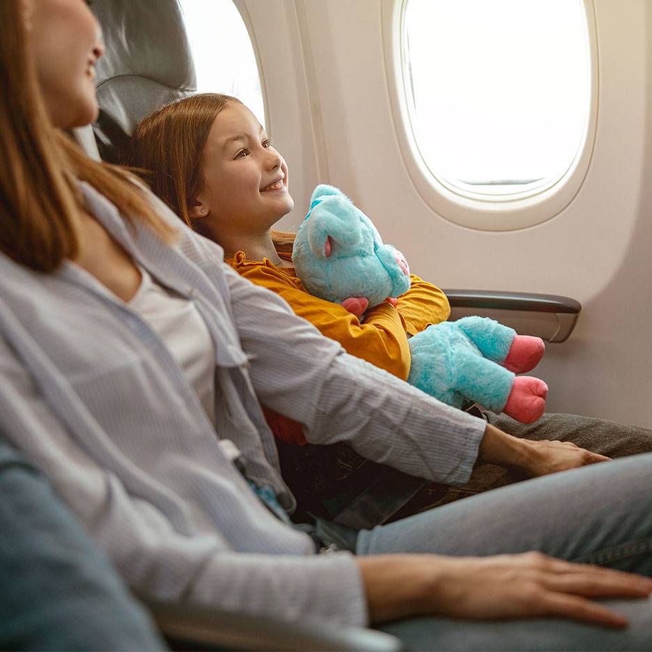 Et barn med et plysdyr kigger ud af et flyvindue ved siden af en voksen.