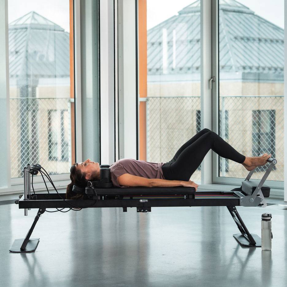 Kvinde laver Pilates-øvelser på en reformer-maskine.