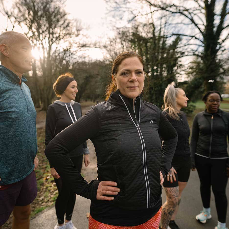 Gruppe mennesker i sportstøj, herunder en kvinde i sort quiltet jakke, udendørs.