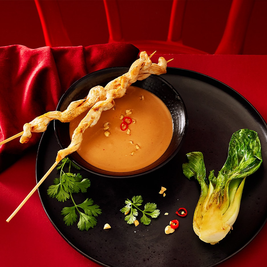 Kyllingespyd med jordnøddesauce, koriander og pak choi på en sort tallerken.