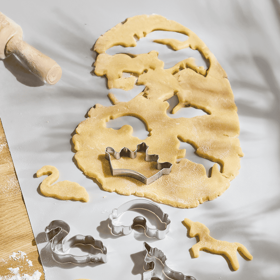 Udrullet småkagedej med udstikkere af en krone, svane, regnbue og enhjørning.