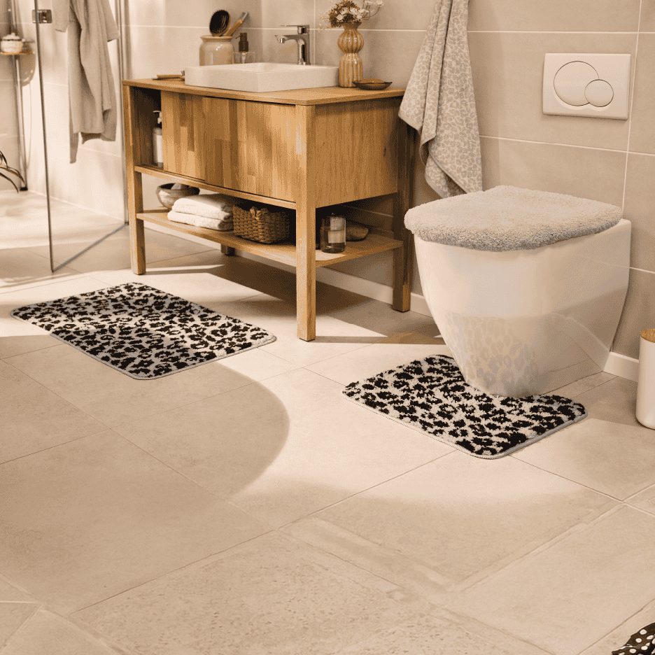 Badeværelse med leopardmønstrede bademåtter, trævaskeskab og toilet.