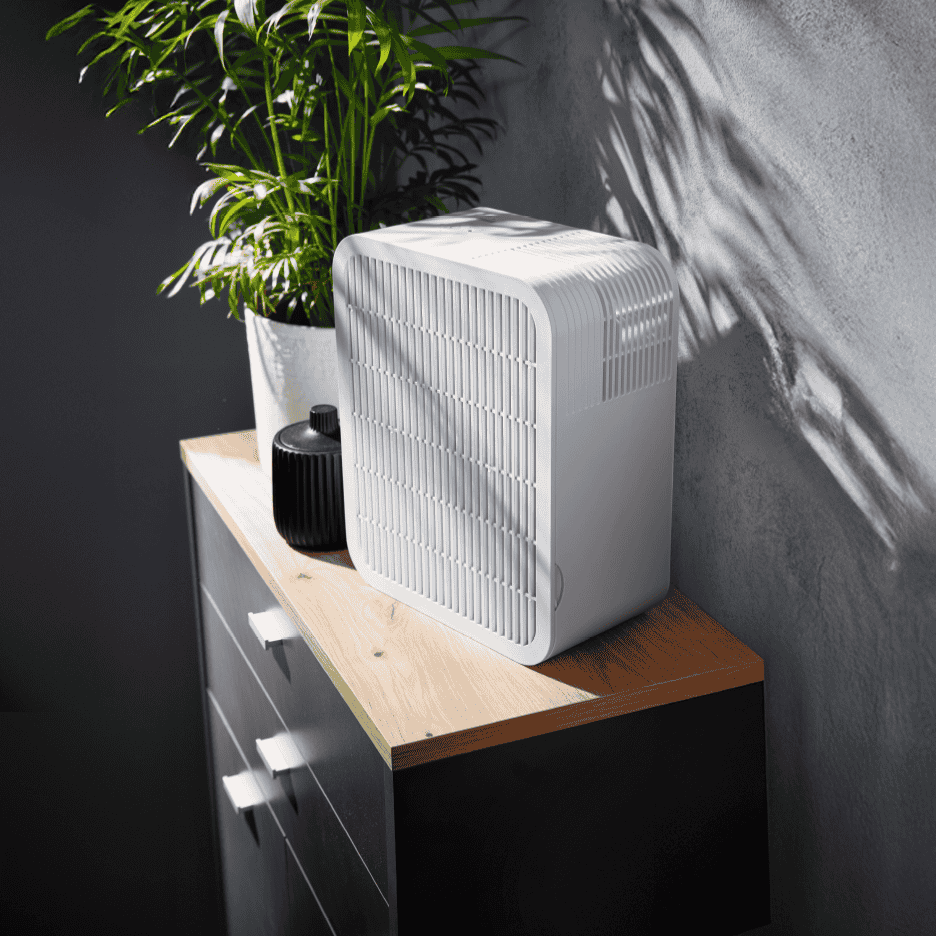 Hvid luftrenser på et træskab ved siden af en grøn plante.