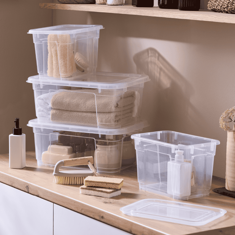 Gennemsigtige opbevaringskasser med låg fyldt med håndklæder og badeværelsesartikler.