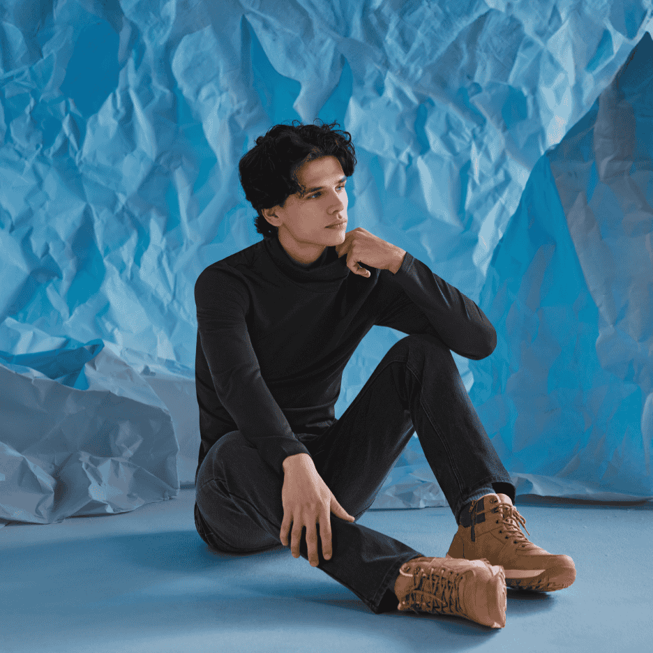 Mand i sort rullekrave og jeans sidder på gulvet med brune støvler.