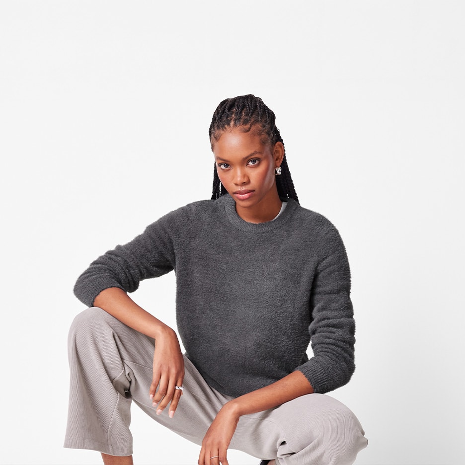 Kvinde i grå fluffy sweater og lyse bukser, der sidder på hug.