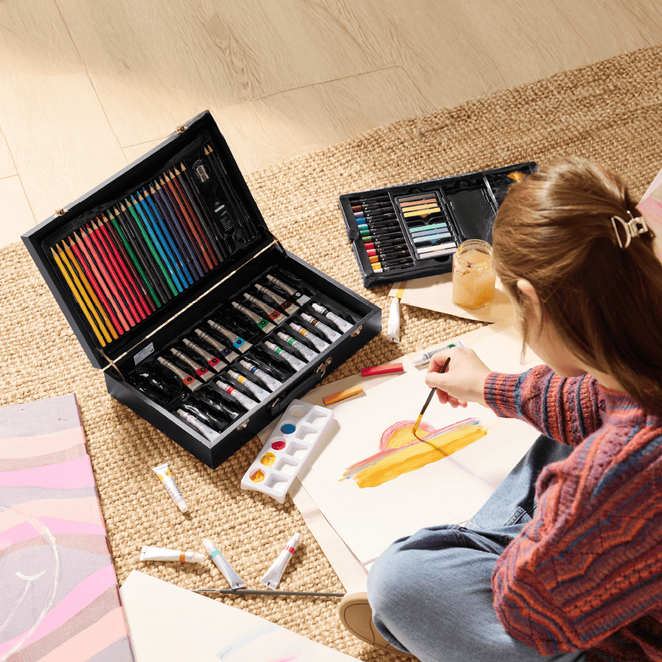 En person maler med et stort kunstsæt med farveblyanter, maling og pasteller.