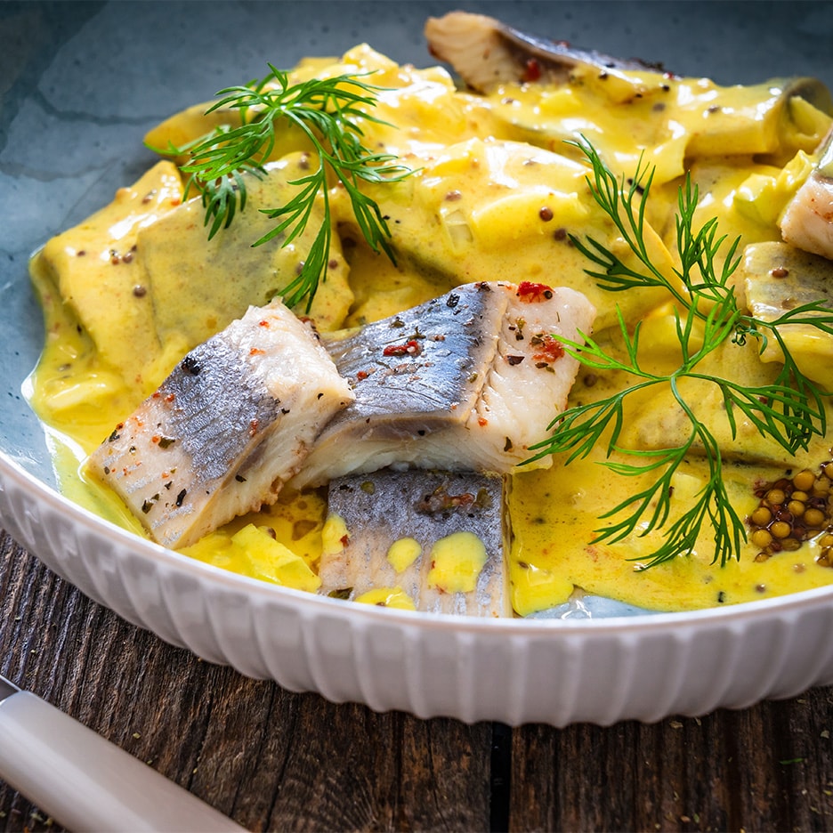 Sild i karrysauce med dild og sennepsfrø i en blå skål på et træbord.