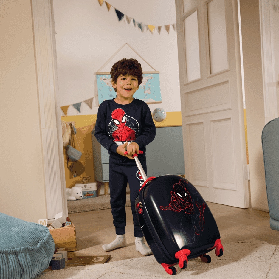 Glad dreng i pyjamas med superhelte-tema trækker en matchende kuffert.