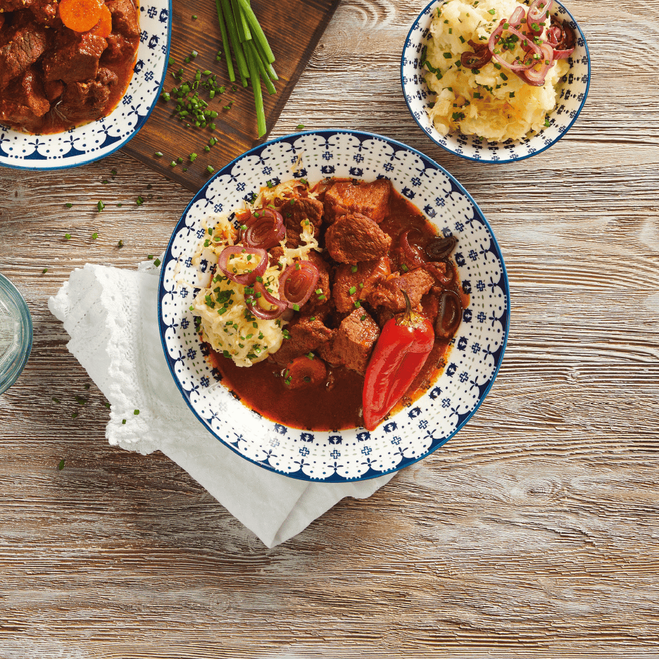 Gryderet med kød, kartoffelmos og rødløg på et træbord.