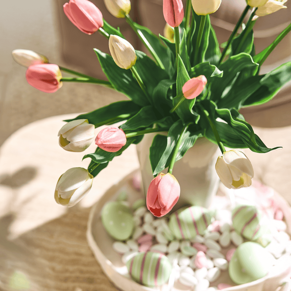En buket lyserøde og hvide tulipaner i en vase med påskeæg og slik på et fad.
