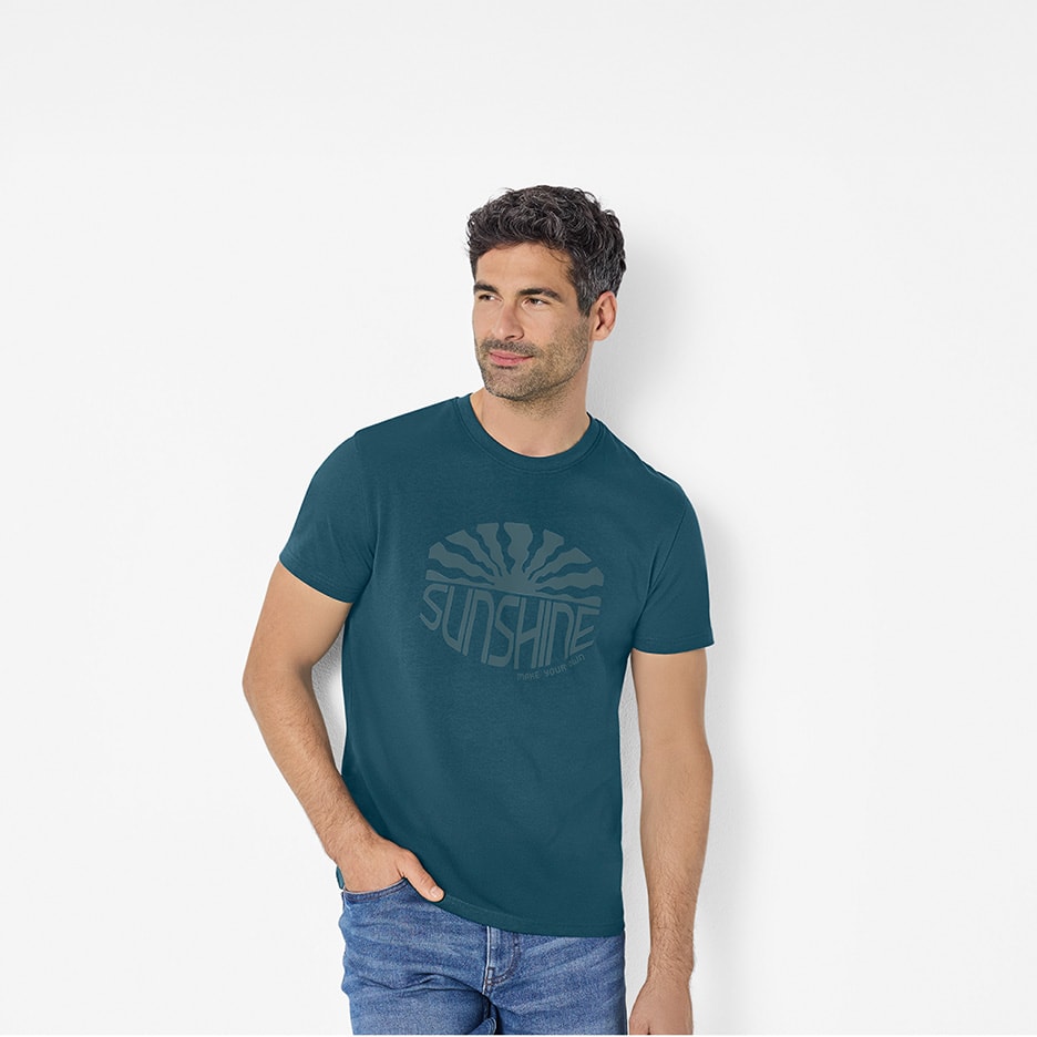 Mand i mørkeblå T-shirt med 'SUNSHINE MAKE YOUR OWN'-print og jeans.