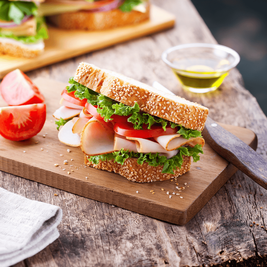 Kalkunsandwich med salat og tomat på et træskærebræt, med olivenolie og tomater.