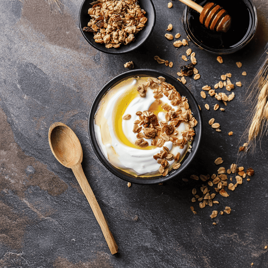 Græsk yoghurt med granola og honning i en sort skål på en mørk stenplade.