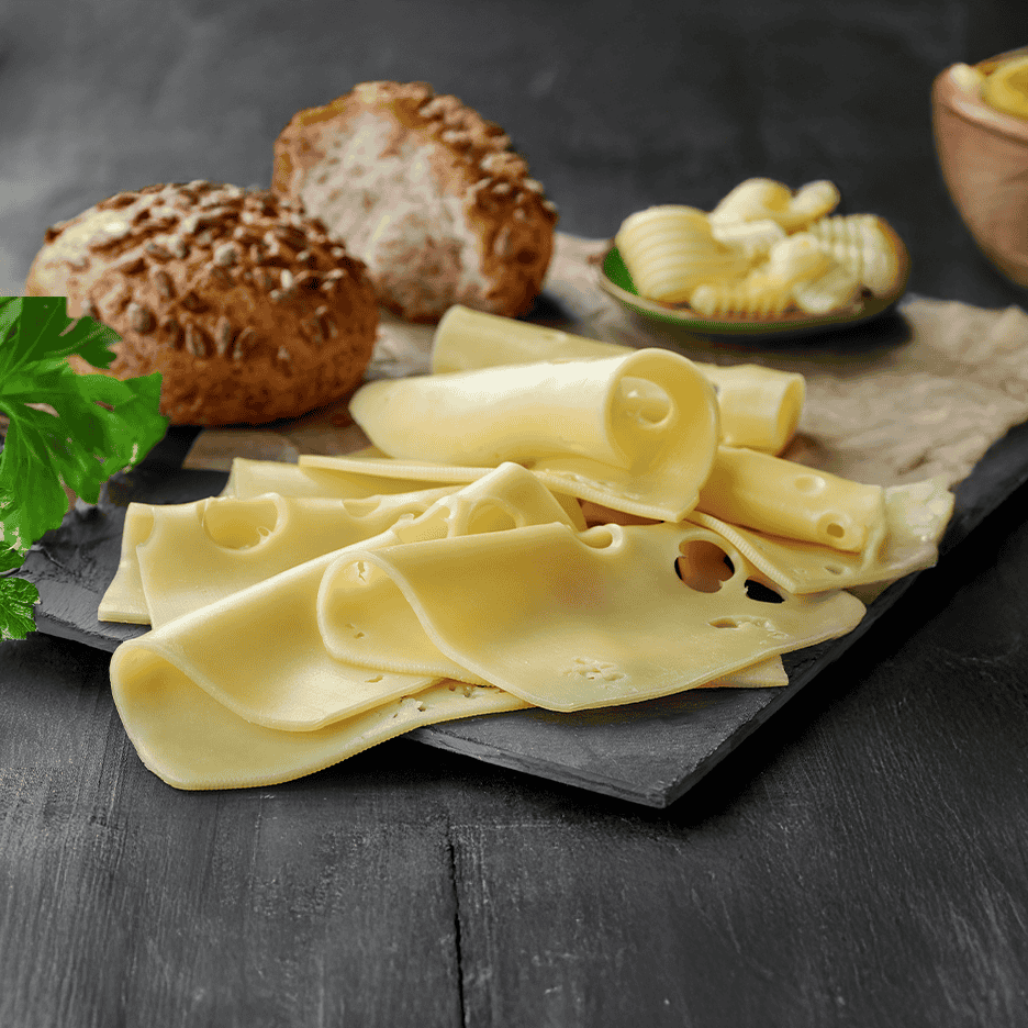 Skiver af ost med huller, brødboller og smørkrøller på et mørkt underlag.