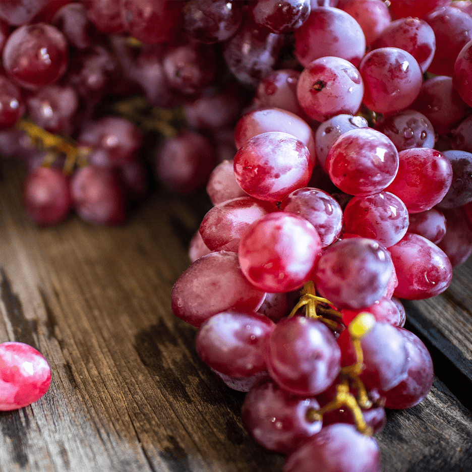 Friske røde druer med vanddråber på en rustik træoverflade.