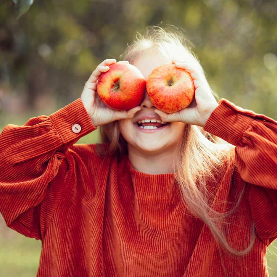 Glad pige med æbler for øjnene i en orange trøje.