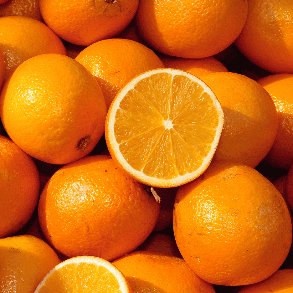 En bunke friske appelsiner, hvoraf én er skåret over og viser frugtkødet.