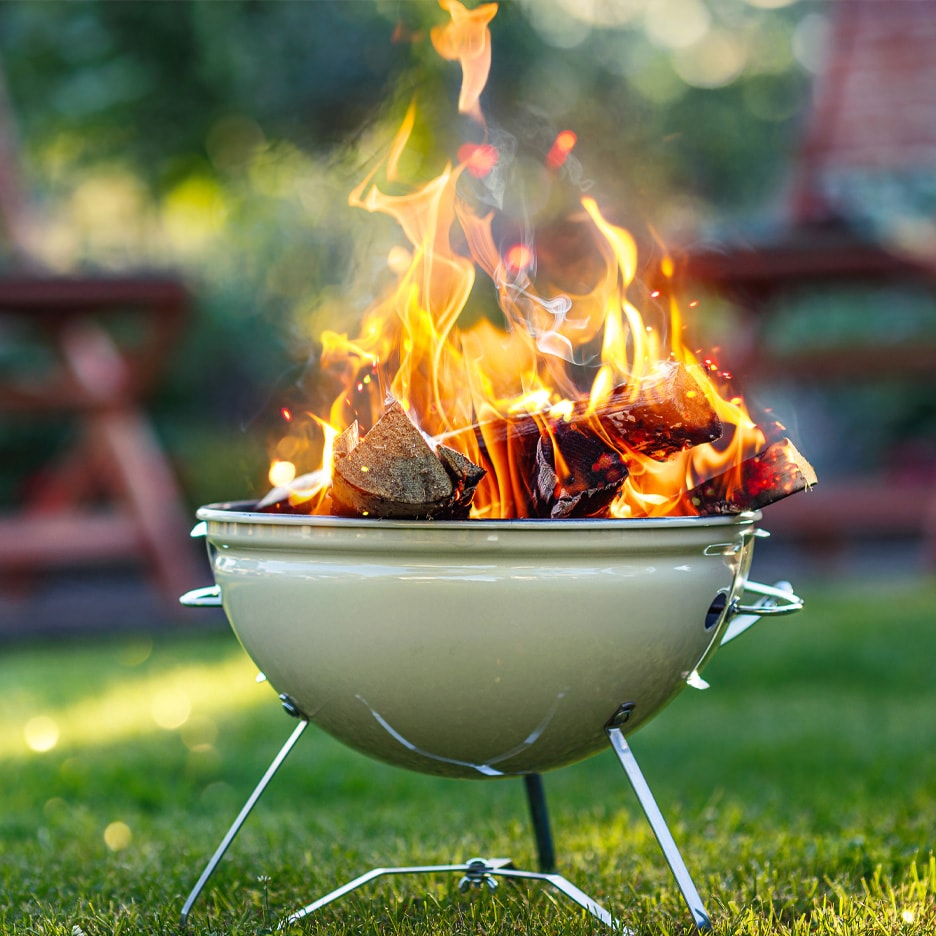 Grill med brændende trækul og flammer i en have.