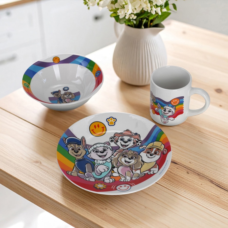 Børneservice med regnbue- og tegneseriefigurer, inklusive en skål, tallerken og krus på et træbord.