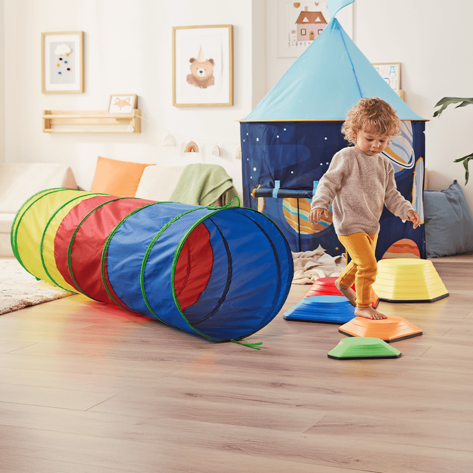 Legetunnel og balancegang i et børneværelse med legetelt og billeder på væggen.