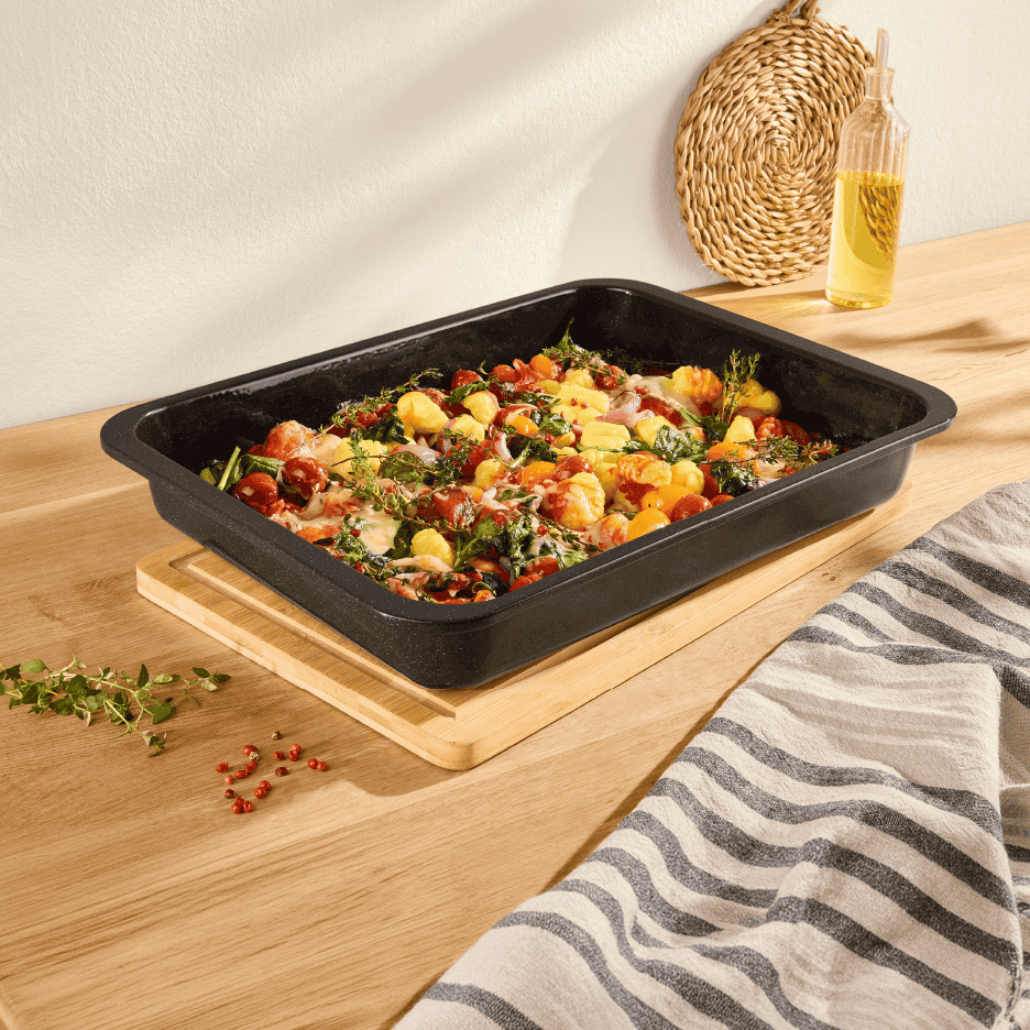 Bageplade med gnocchi, grøntsager og krydderurter på et træbord.