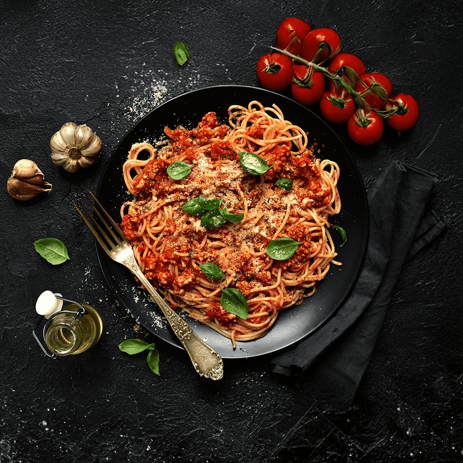 Spaghetti bolognese med tomater, hvidløg og basilikum på sort baggrund.