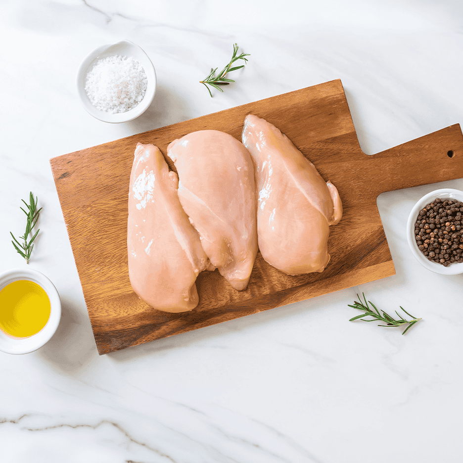 Rå kyllingebrystfileter på skærebræt med rosmarin, salt og peberkorn.