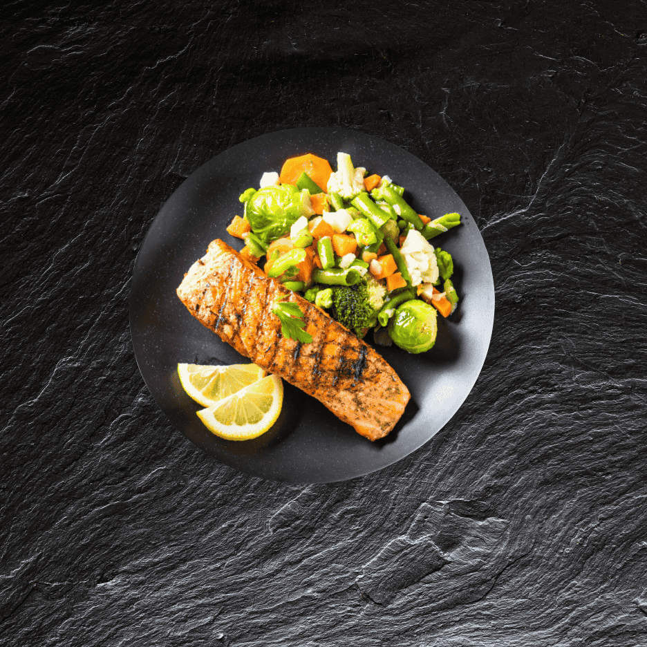 Grillet laks med dampede grøntsager og citron på en sort tallerken.