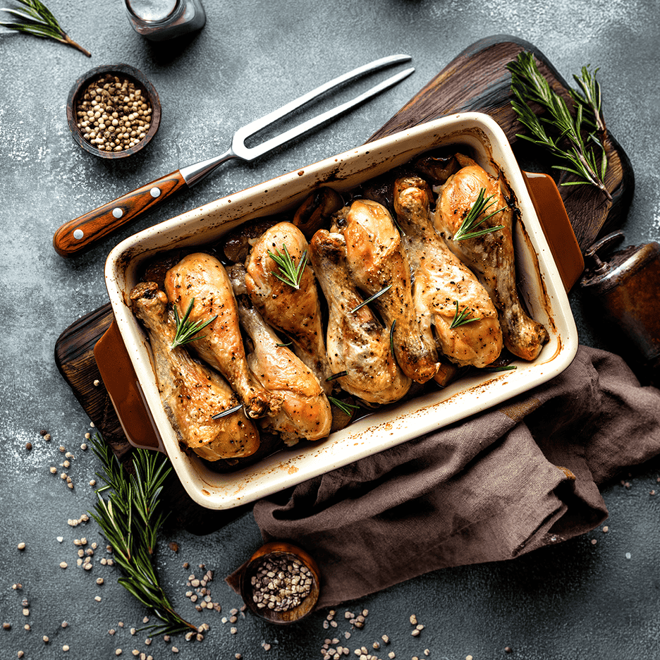 Ovnbagte kyllingelår med rosmarin og peberkorn i et fad på et mørkt underlag.