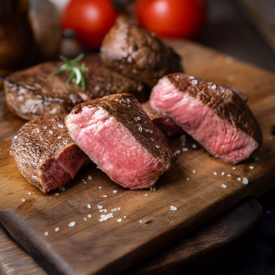 Saftige bøffer med havsalt og rosmarin på et træskærebræt.