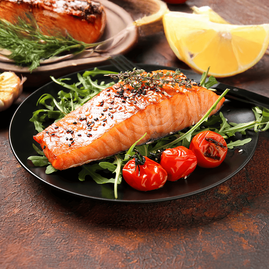 Laks med sesamfrø, rucola og grillede tomater på en sort tallerken.