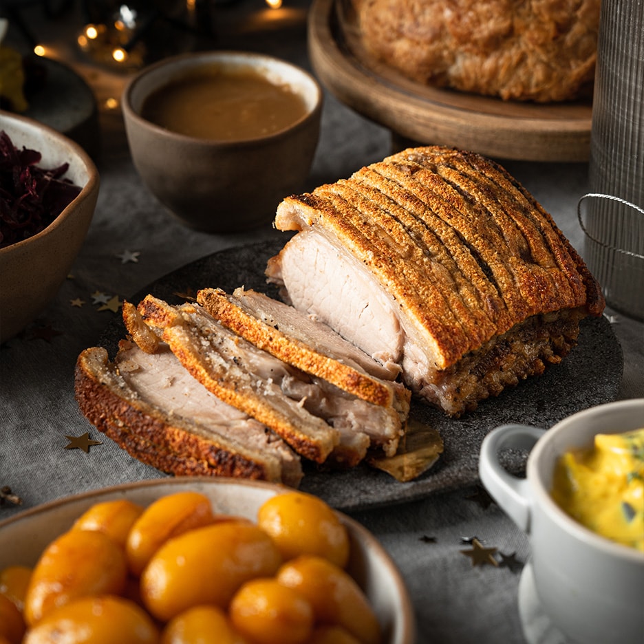 Skiver af sprødstegt flæskesteg med tilbehør som kartofler og sovs på et festligt bord.