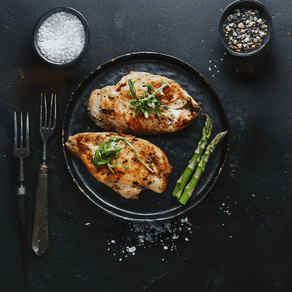 Grillet kyllingebryst med asparges og krydderier på en mørk tallerken.