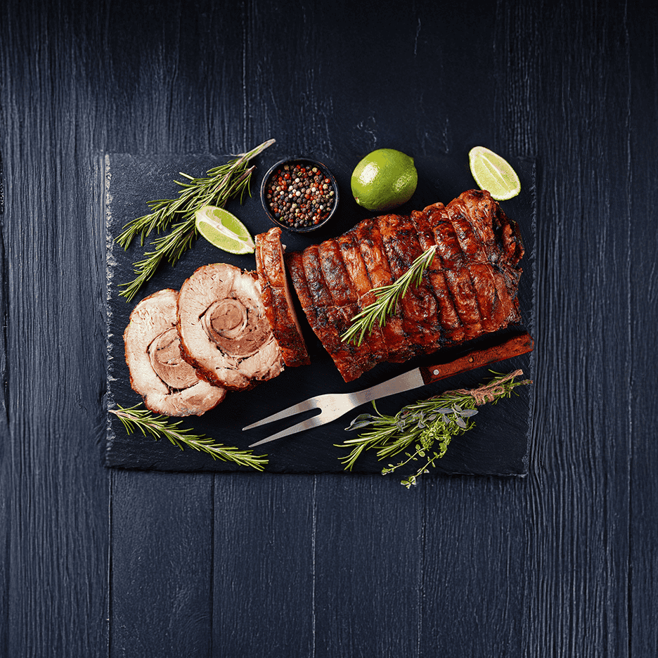 Skiver af stegt kød med rosmarin, lime og peberkorn på en sort skiferplade.