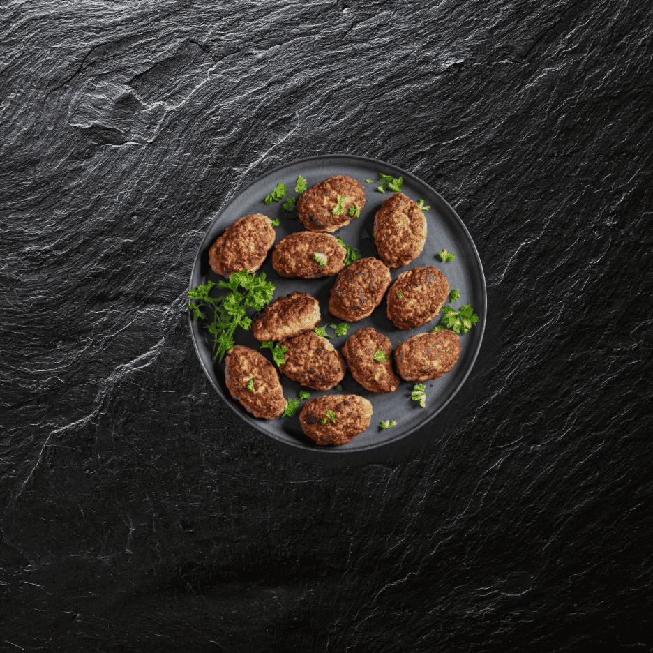 Frikadeller med persille på en mørk tallerken på en sort skiferbaggrund.