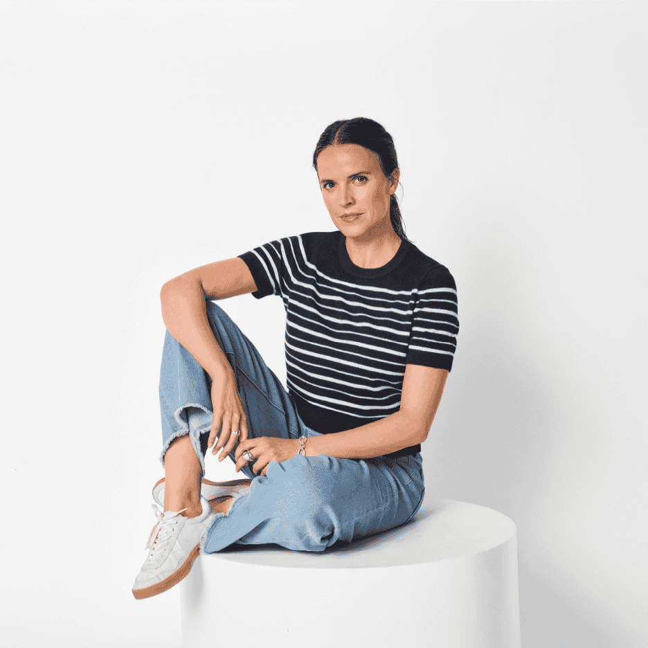 Kvinde i stribet T-shirt og jeans sidder på en hvid cylinder.